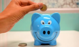 Hand inserting a coin into a blue piggy bank for savings and money management.