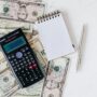 Flat lay of US dollar bills with calculator and notebook for budgeting.