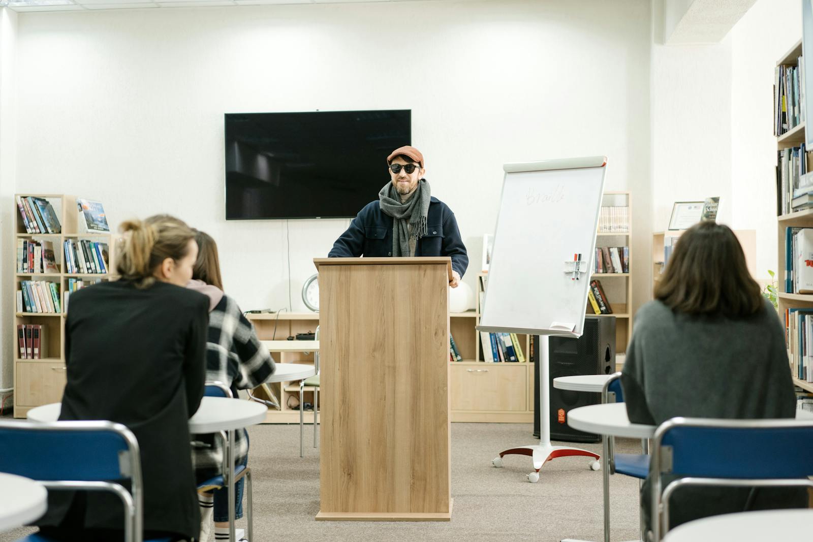 A blind instructor using a cane teaches students in a classroom setting.