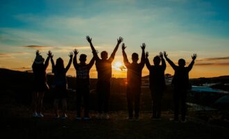 A diverse group of friends raises their arms in celebration against a vibrant sunset backdrop.