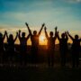 A diverse group of friends raises their arms in celebration against a vibrant sunset backdrop.