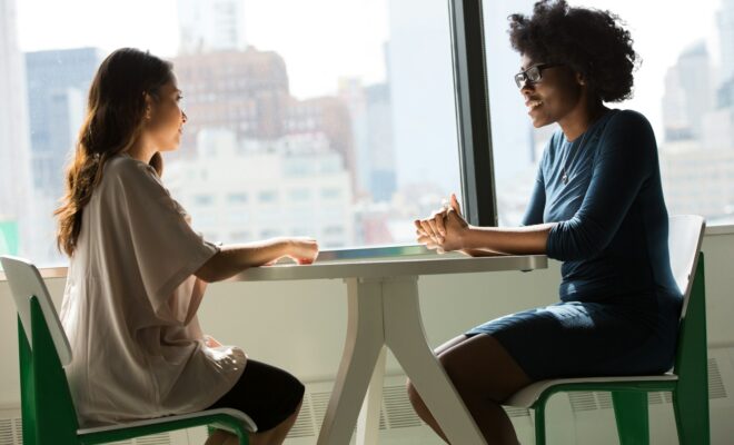 two women sitting beside table and talking