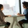 two women sitting beside table and talking